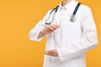 Photo of Doctor with stethoscope holding something on orange background, closeup. Space for text