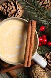 Photo of Tasty eggnog, cinnamon sticks and fir branches on wooden table, flat kay