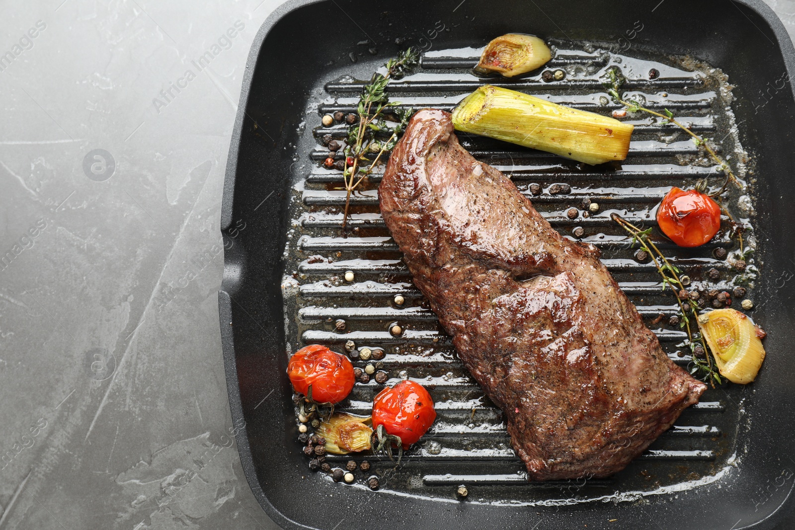 Photo of Delicious grilled beef meat and vegetables in pan on grey table, top view. Space for text