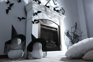 Photo of Beautiful black witch hats on pumpkins near fireplace indoors. Halloween celebration