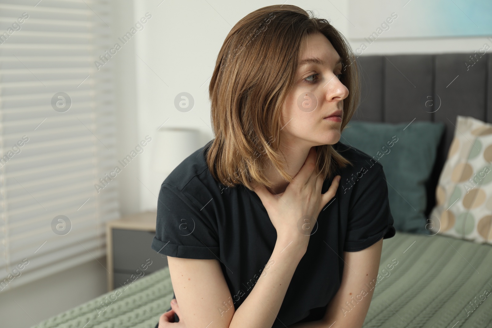 Photo of Sad young woman sitting on bed at home