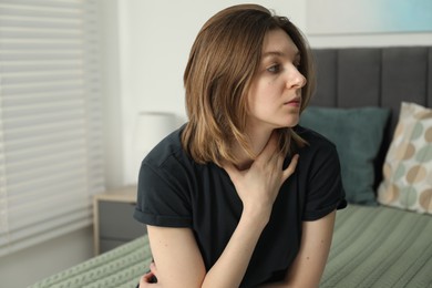 Sad young woman sitting on bed at home