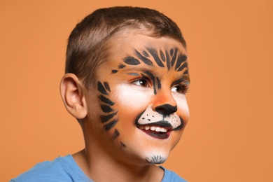 Photo of Cute little boy with face painting on orange background