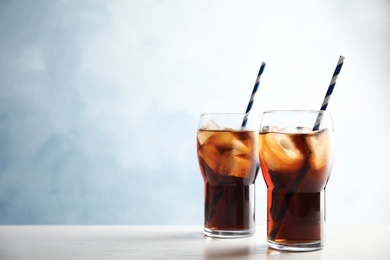 Glasses of refreshing cola with ice cubes and straws on table. Space for text