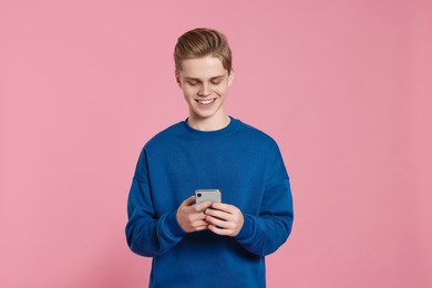 Teenage boy using smartphone on pink background