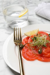 Photo of Salmon carpaccio with capers, microgreens and lemon served on white marble table, closeup