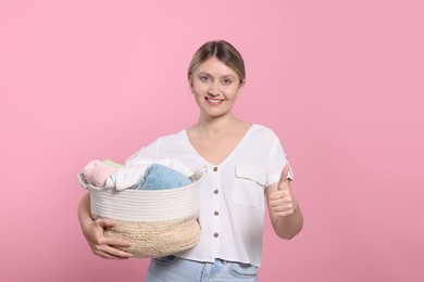 Happy woman with basket full of laundry showing thumb up on pink background