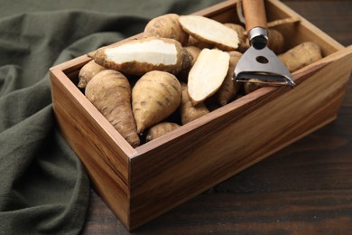 Photo of Tubers of turnip rooted chervil and peeler in crate on wooden table, closeup