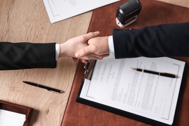 Photo of Notary shaking hands with client at wooden table, top view