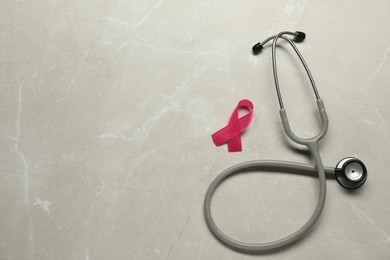 Breast cancer awareness. Pink ribbon and stethoscope on light grey table, flat lay. Space for text