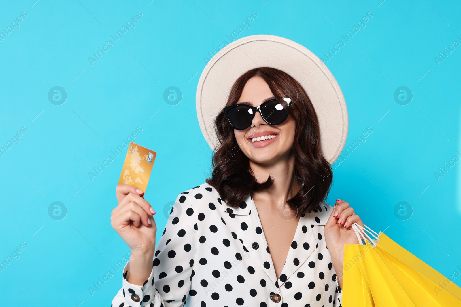 Photo of Beautiful young woman with paper shopping bags and credit card on light blue background