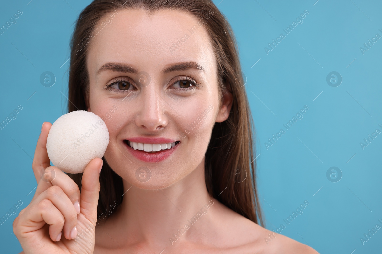 Photo of Happy young woman holding face sponge on light blue background
