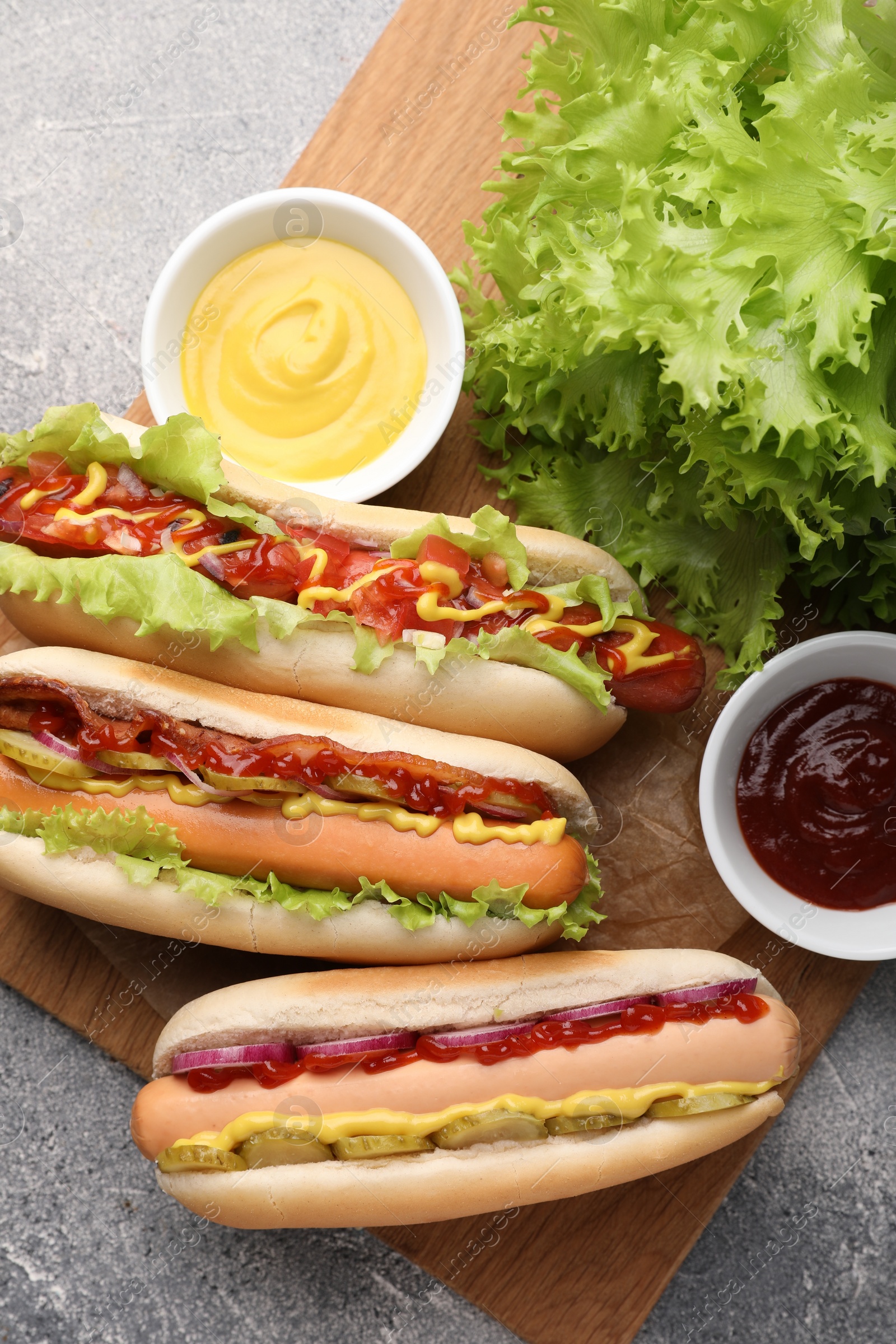 Photo of Delicious hot dogs with different toppings served on grey table, flat lay