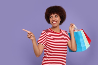 Photo of Happy young woman with shopping bags pointing at something on purple background. Space for text