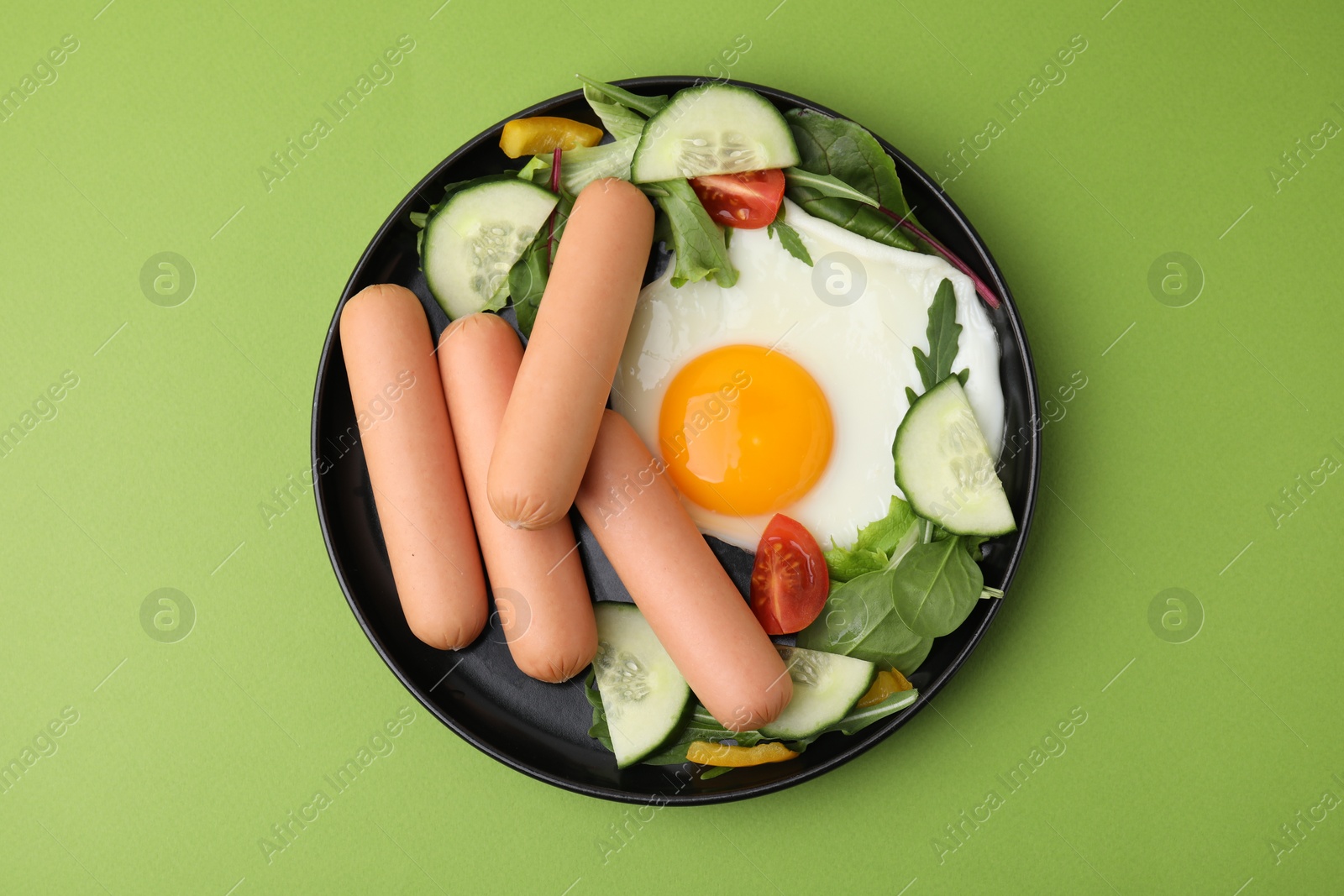 Photo of Delicious breakfast with boiled sausages and fried egg on green background, top view