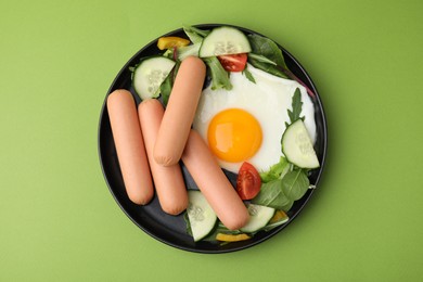 Delicious breakfast with boiled sausages and fried egg on green background, top view