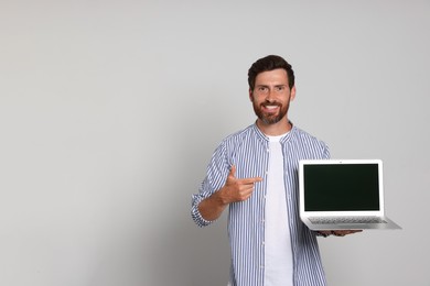 Handsome man pointing at laptop on light background