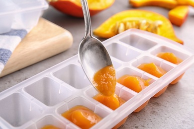 Photo of Putting healthy baby food into ice cube tray, closeup