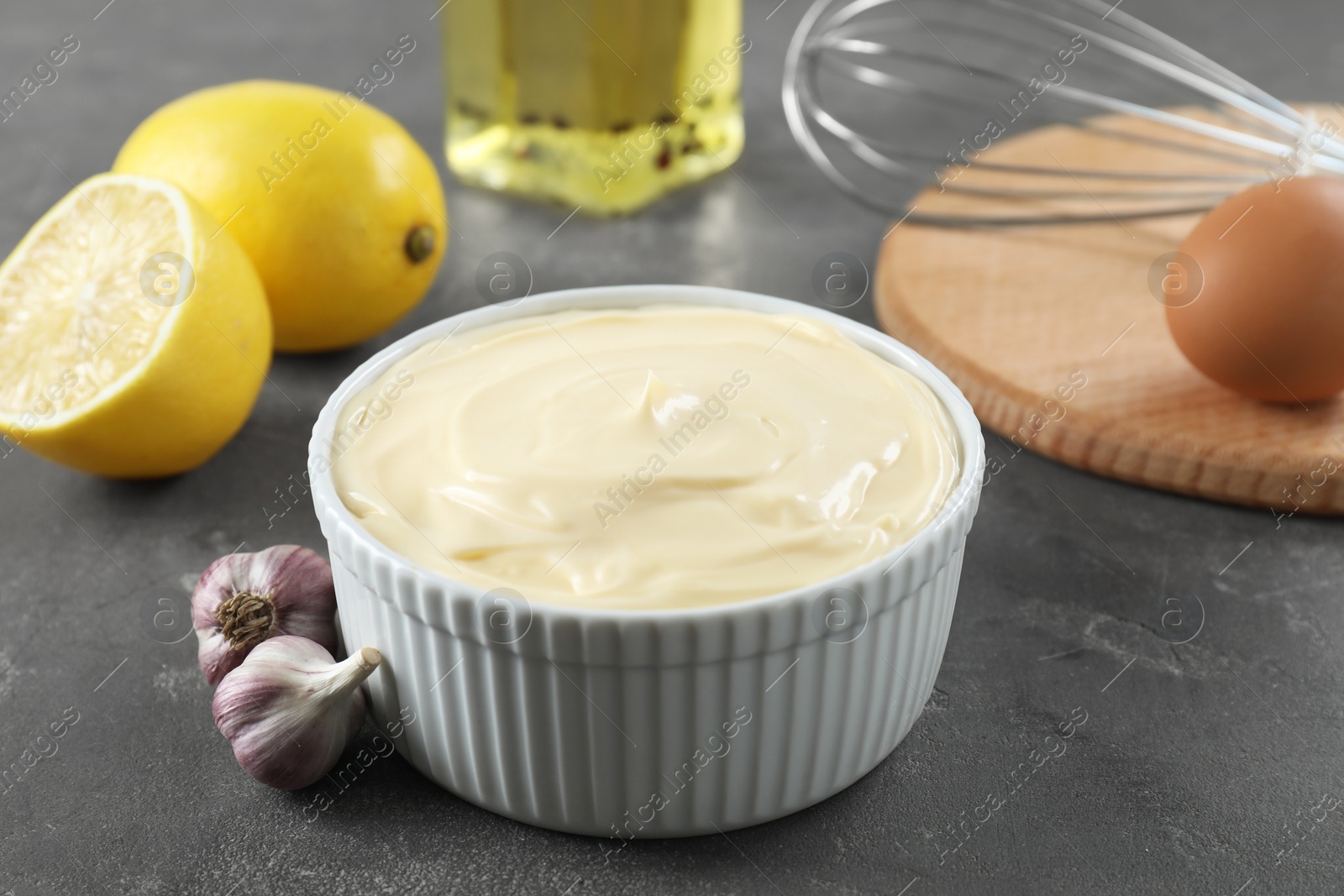 Photo of Fresh mayonnaise sauce in bowl and ingredients on grey table