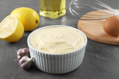 Photo of Fresh mayonnaise sauce in bowl and ingredients on grey table