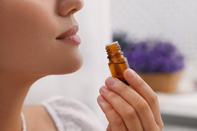 Woman with bottle of essential oil indoors, closeup