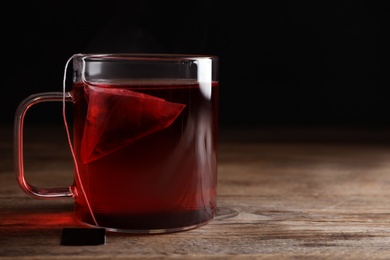 Photo of Tea bag in cup of hot water on wooden table. Space for text