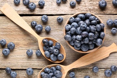 Photo of Spoons and bowl with tasty fresh blueberries on wooden table, flat lay
