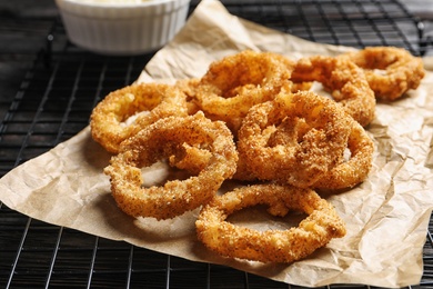 Photo of Cooling rack with homemade crunchy fried onion rings on wooden background, closeup