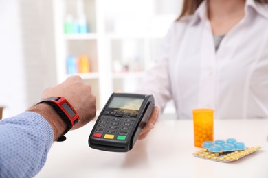 Photo of Man using terminal for contactless payment with smart watch in pharmacy, closeup. Space for text