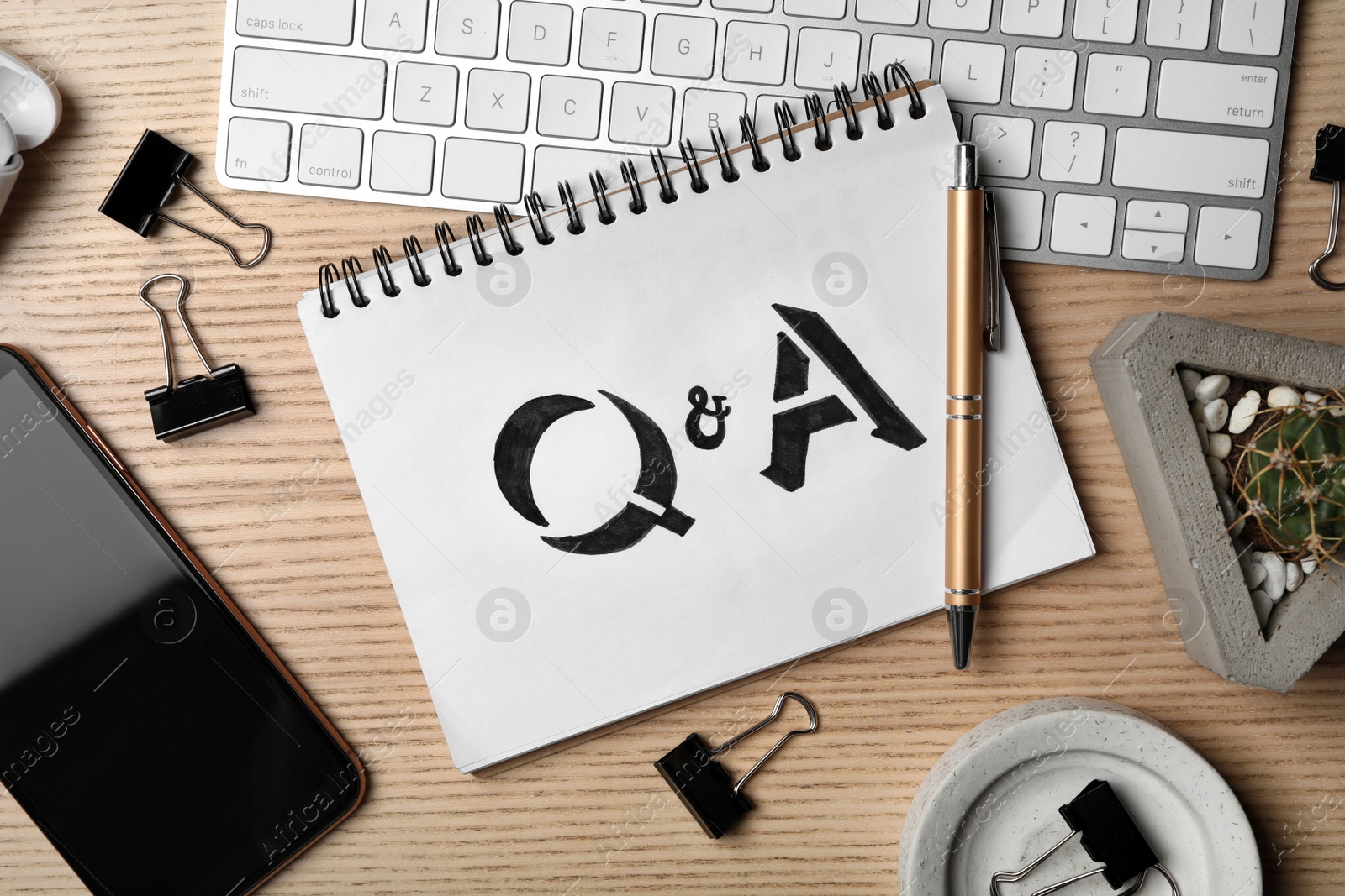 Photo of Notebook with text Q&A, keyboard and smartphone on wooden table, flat lay