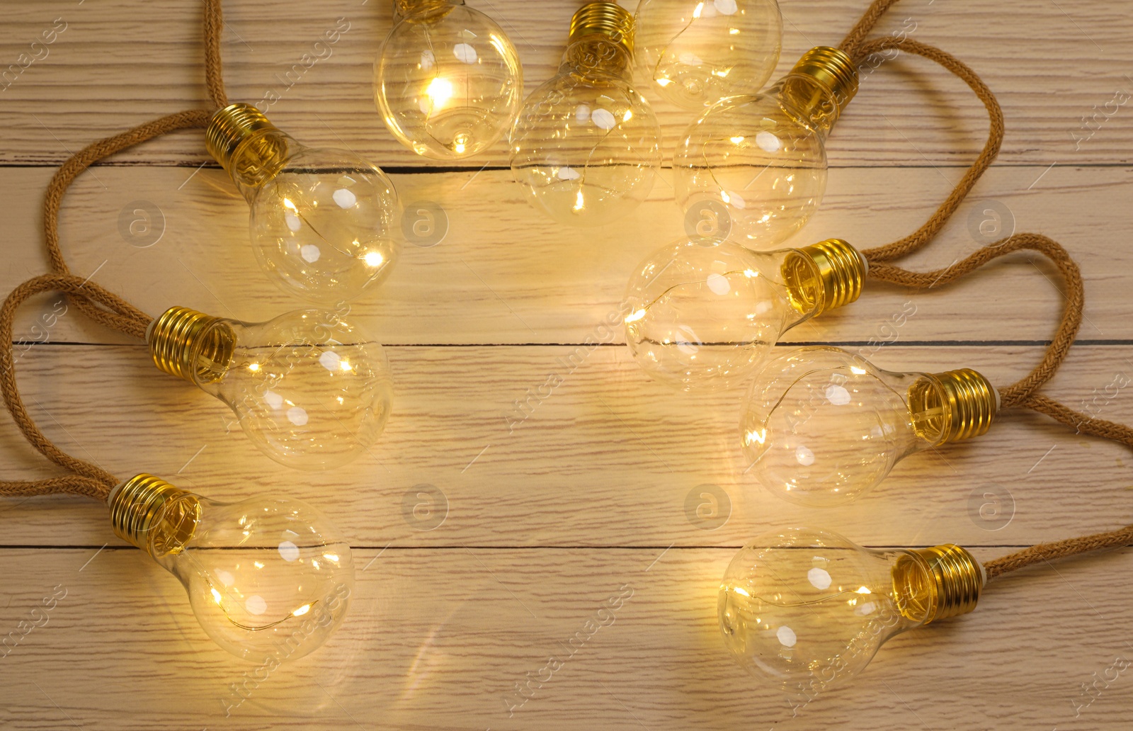 Photo of String lights with lamp bulbs on wooden background, top view