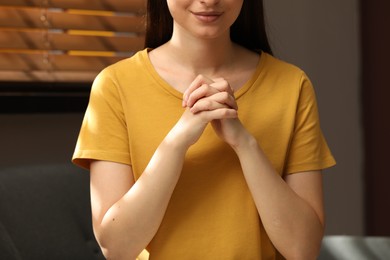 Religious woman with clasped hands praying indoors, closeup
