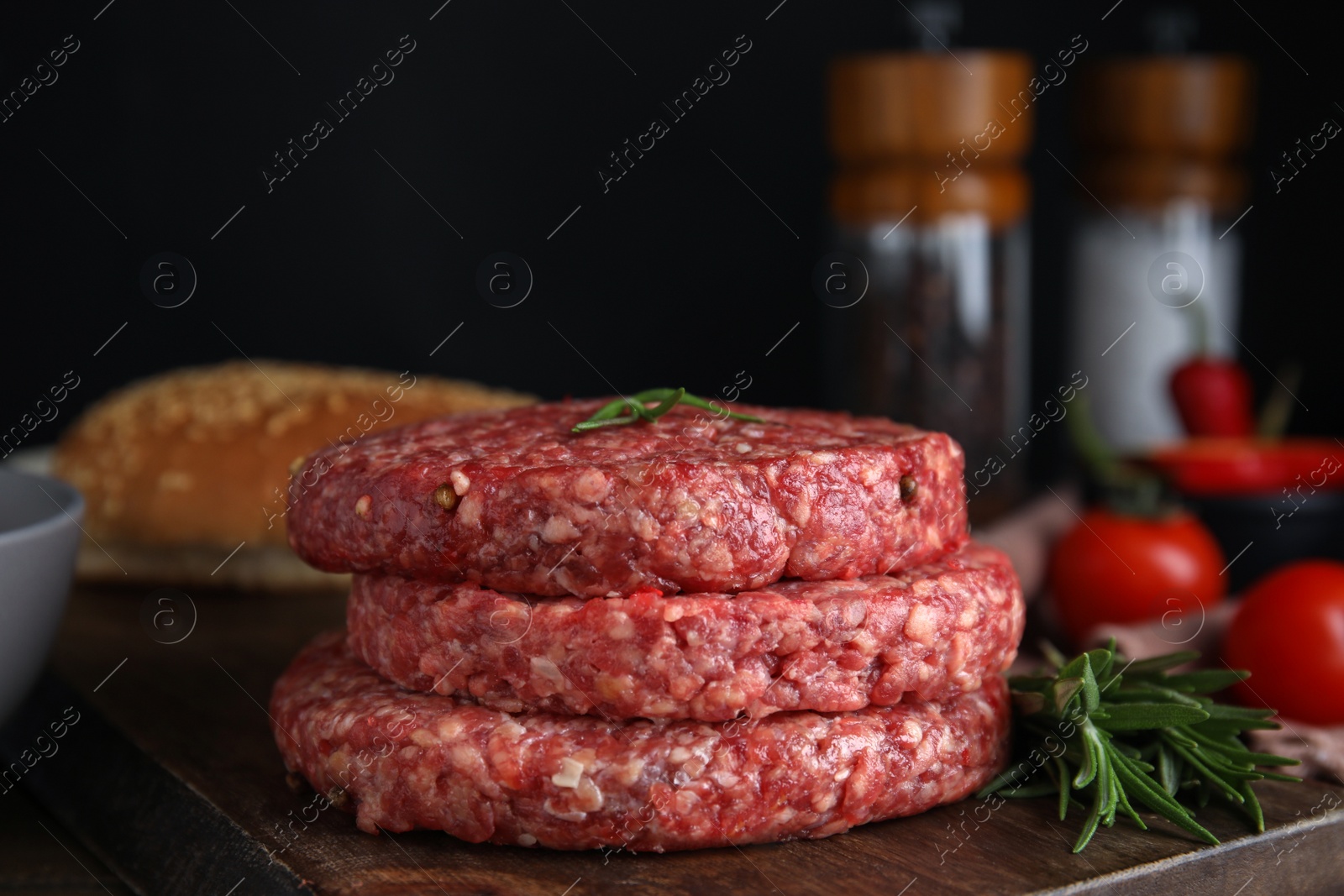 Photo of Raw hamburger patties with rosemary on wooden board, closeup