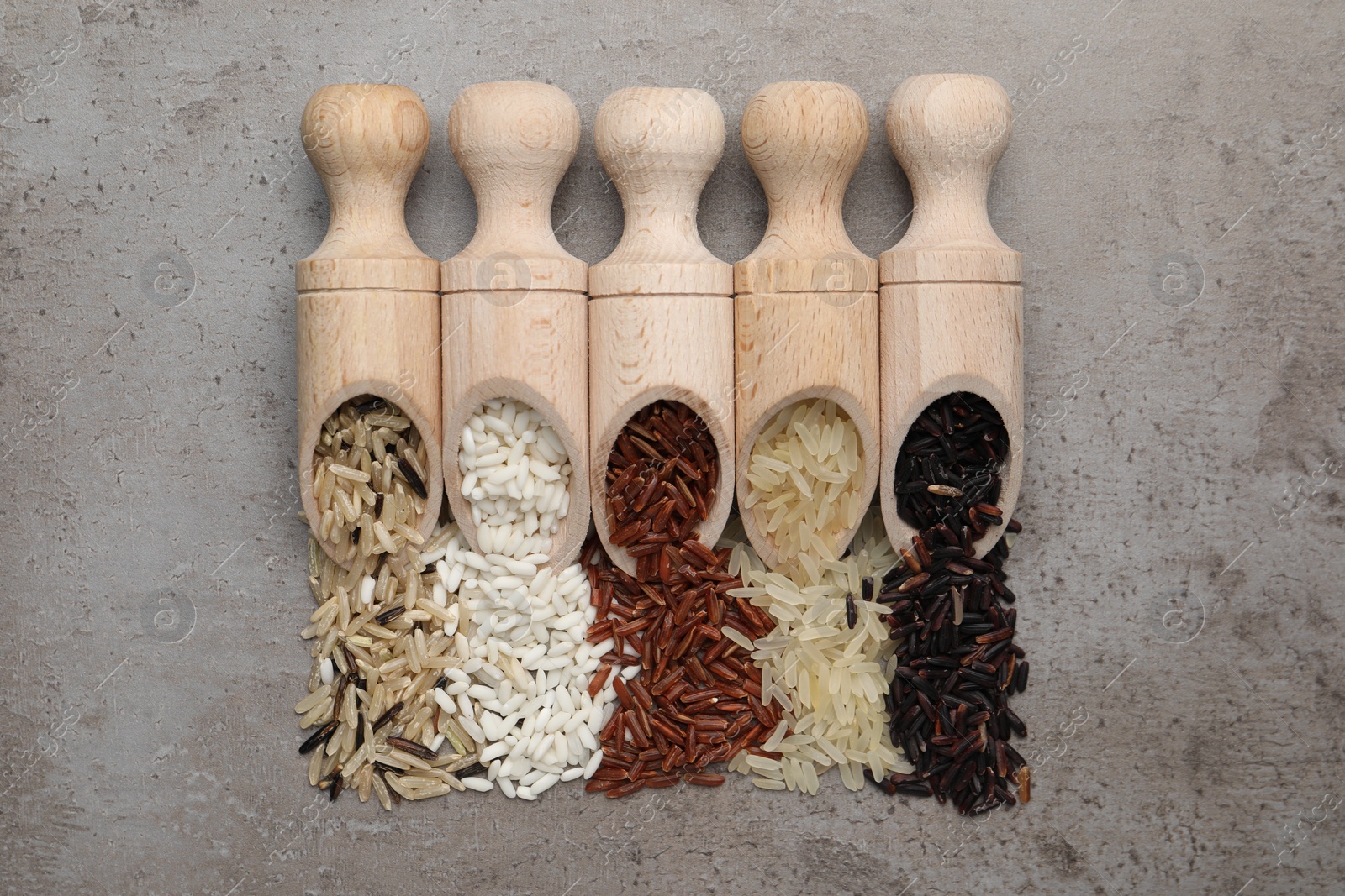 Photo of Scoops with different sorts of rice on grey table, flat lay