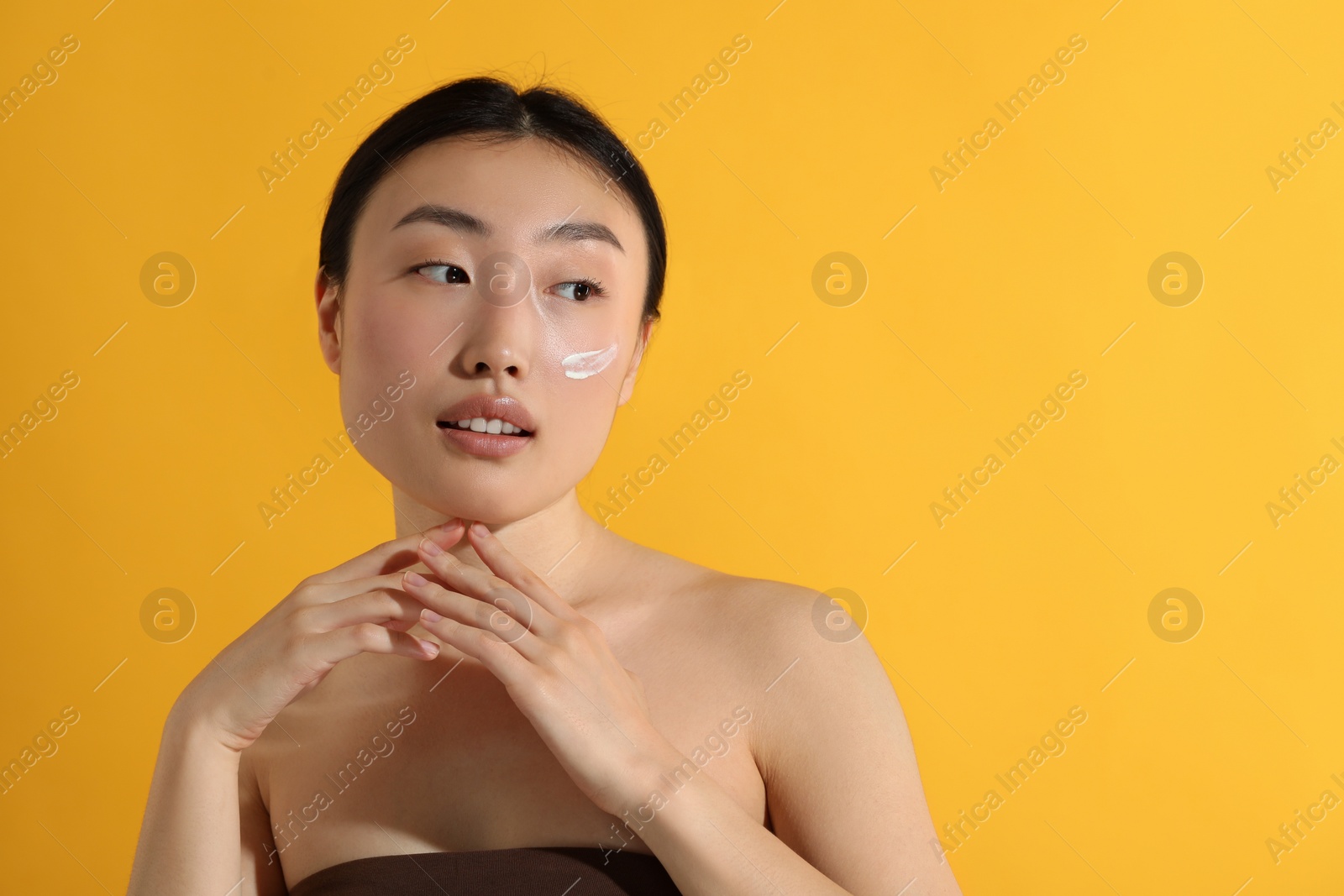 Photo of Beautiful young woman with sun protection cream on her face against orange background, space for text