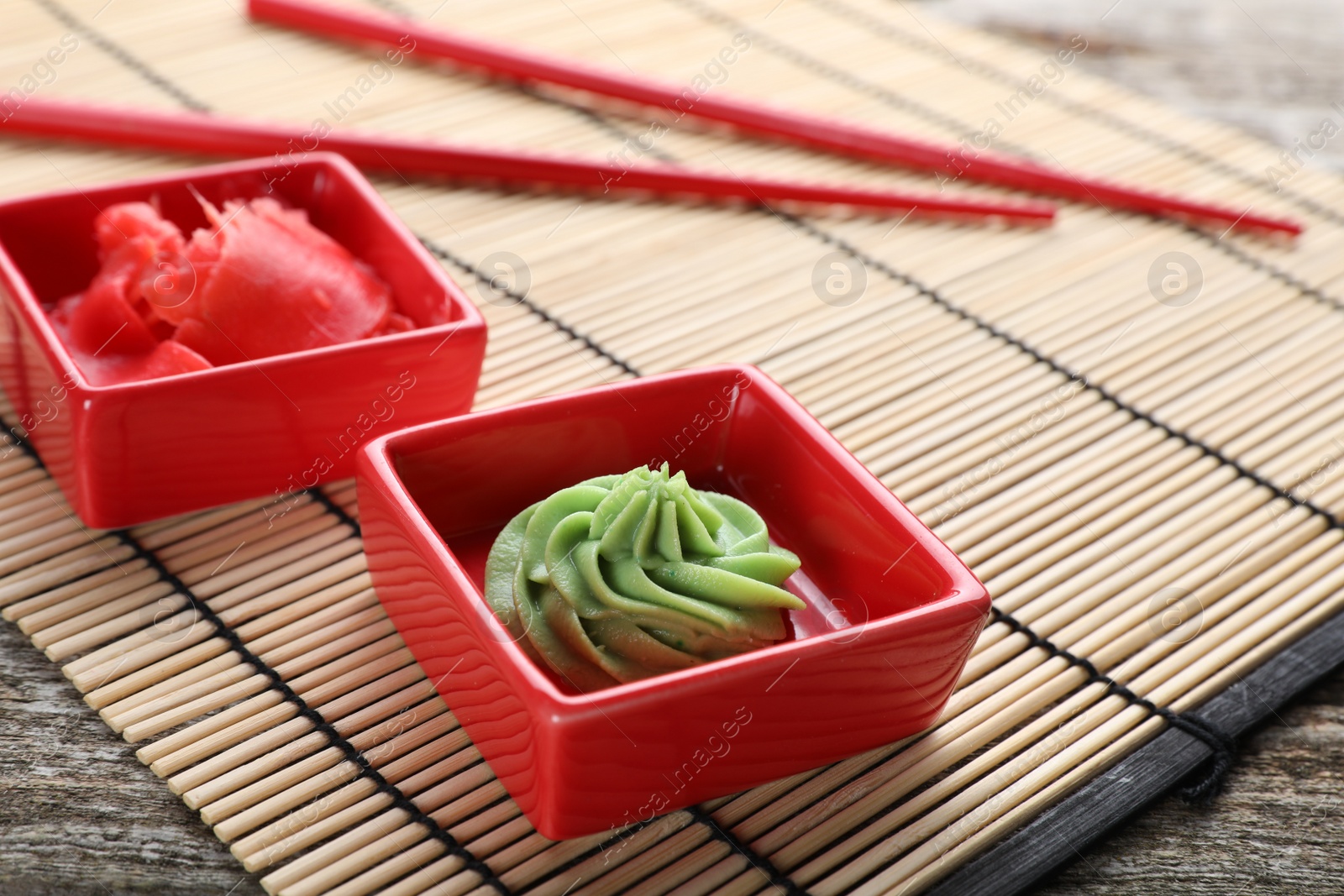 Photo of Bowls with swirl of wasabi paste and pickled ginger on bamboo mat, closeup