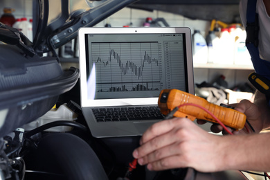 Mechanic with laptop doing car diagnostic at automobile repair shop, closeup
