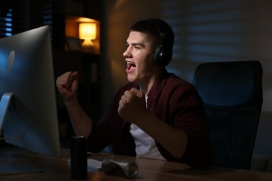 Emotional man playing video games on computer at table indoors
