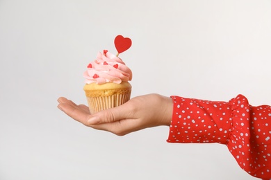 Woman holding tasty cupcake for Valentine's Day on light background, closeup