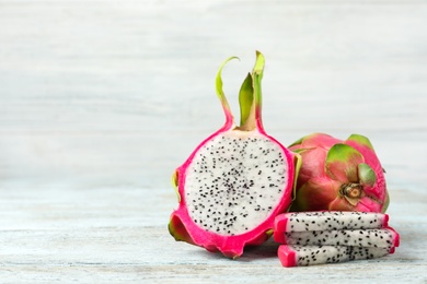 Delicious cut and whole dragon fruits (pitahaya) on light wooden table. Space for text