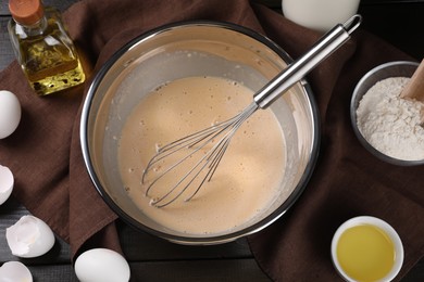 Flat lay composition with whisk and dough in bowl on wooden table