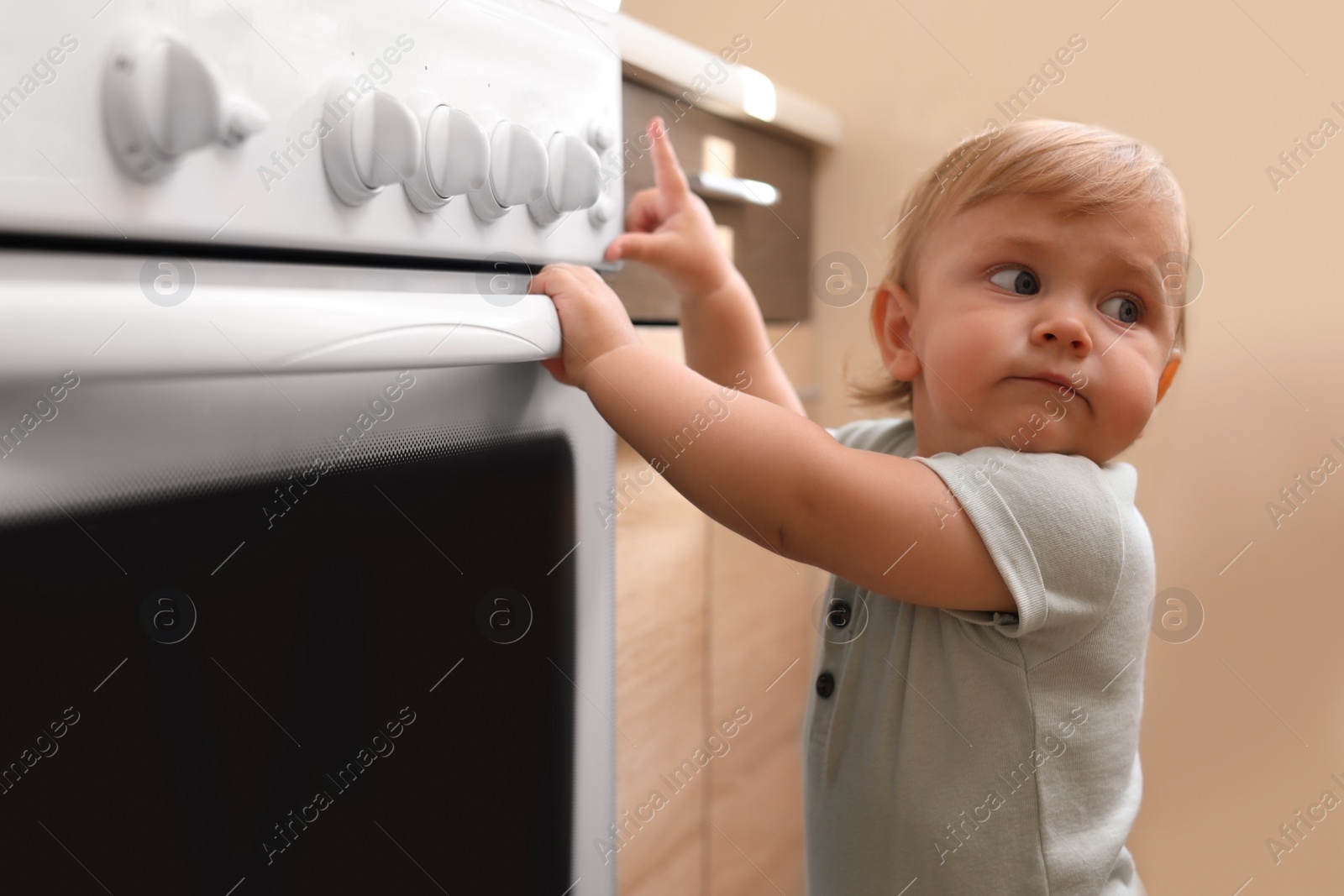 Photo of Little child playing with gas stove indoors. Dangers in kitchen