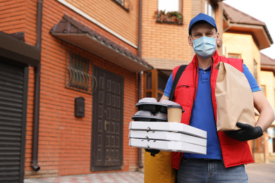 Courier in protective mask and gloves with orders near house outdoors. Food delivery service during coronavirus quarantine