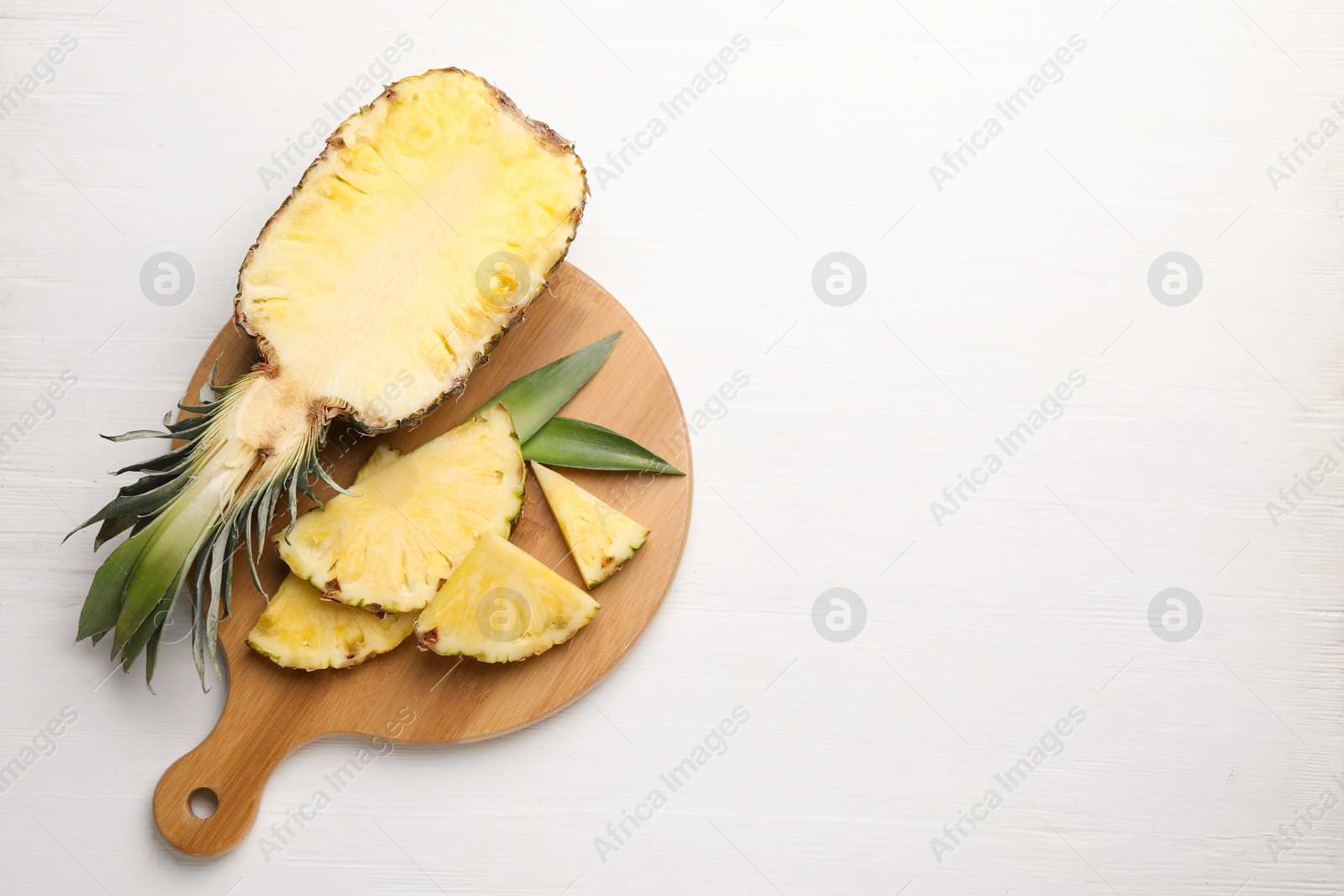 Photo of Ripe juicy pineapple on white wooden table, top view. Space for text