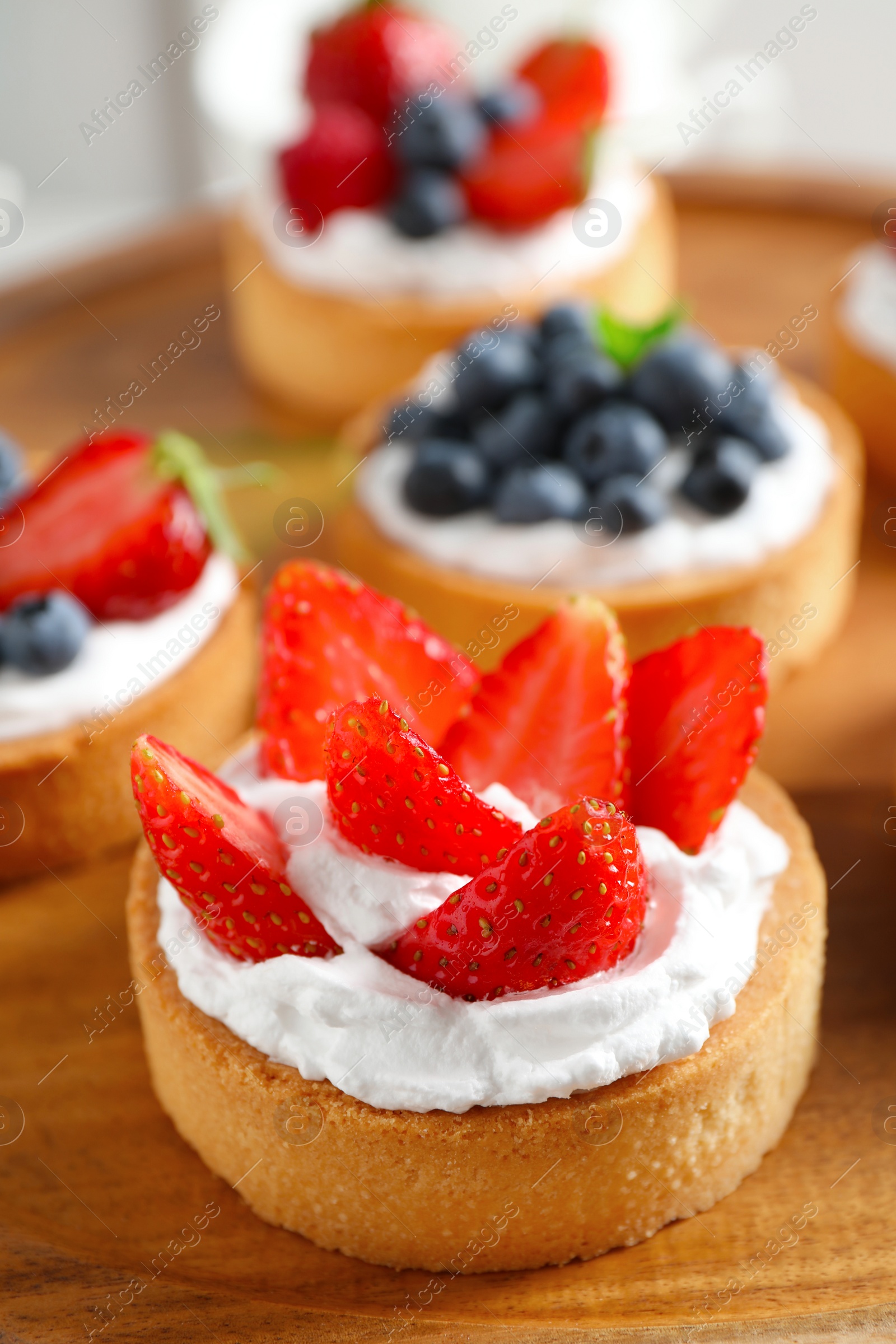 Photo of Wooden plate with different berry tarts. Delicious pastries