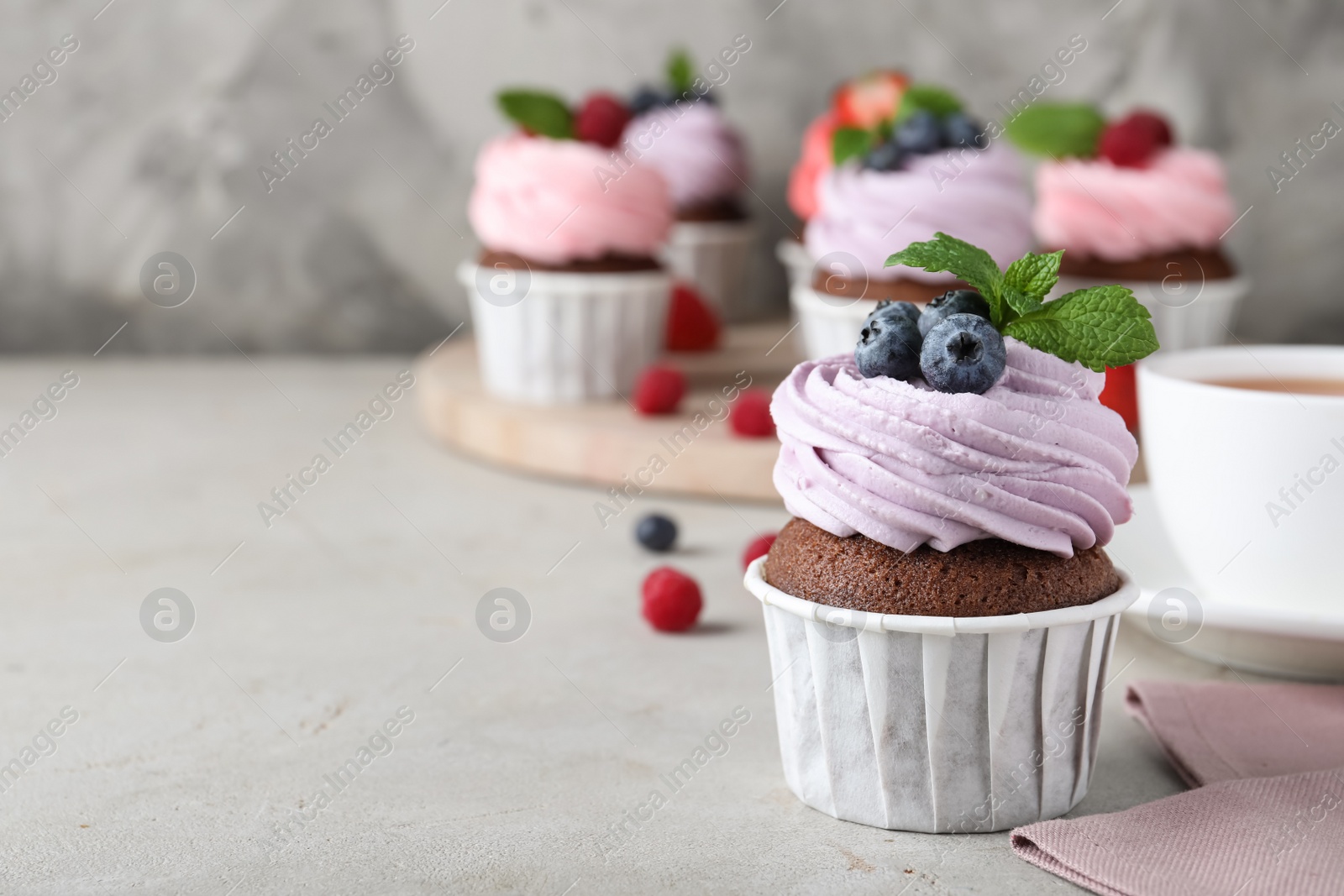 Photo of Delicious cupcake with cream and blueberries on light grey table, space for text