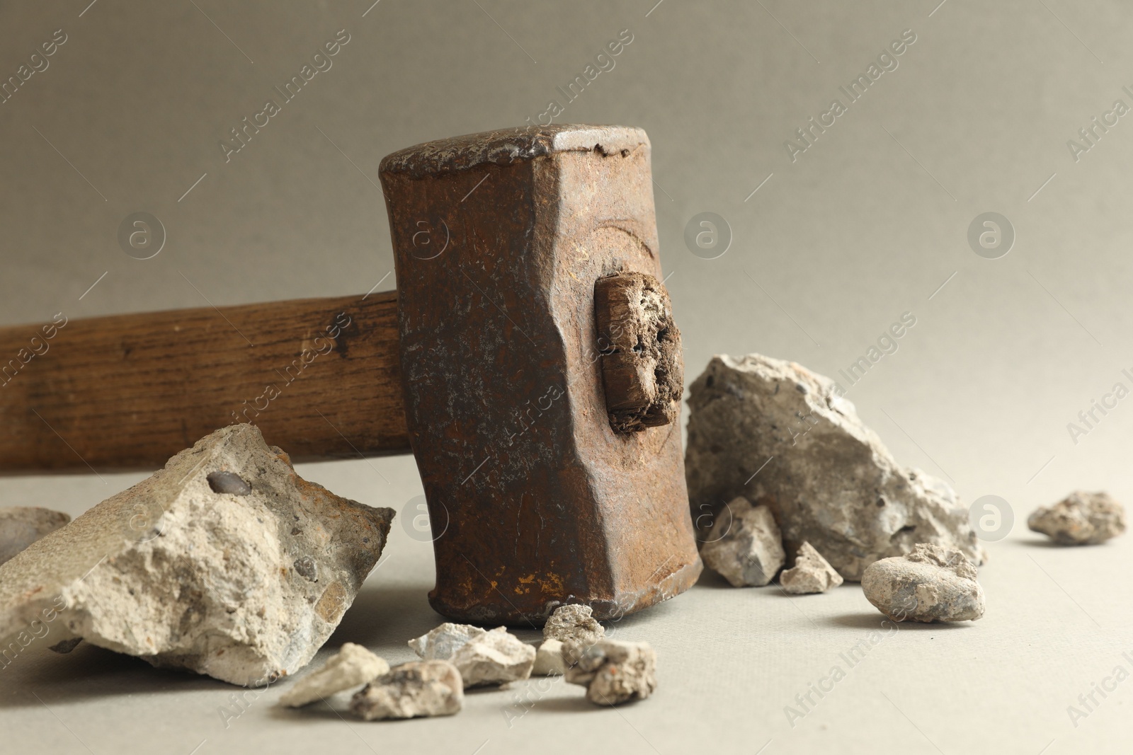 Photo of One sledgehammer and pieces of broken stones on grey background, closeup