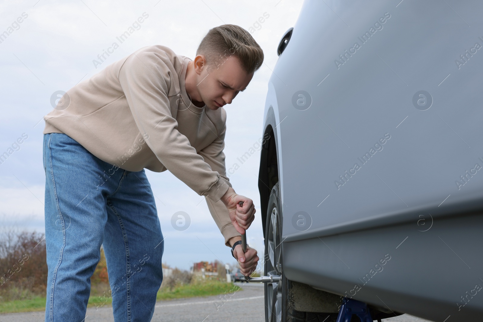 Photo of Young man changing tire of car on roadside