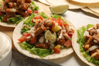 Photo of Delicious tacos with vegetables, meat and lime on table, closeup