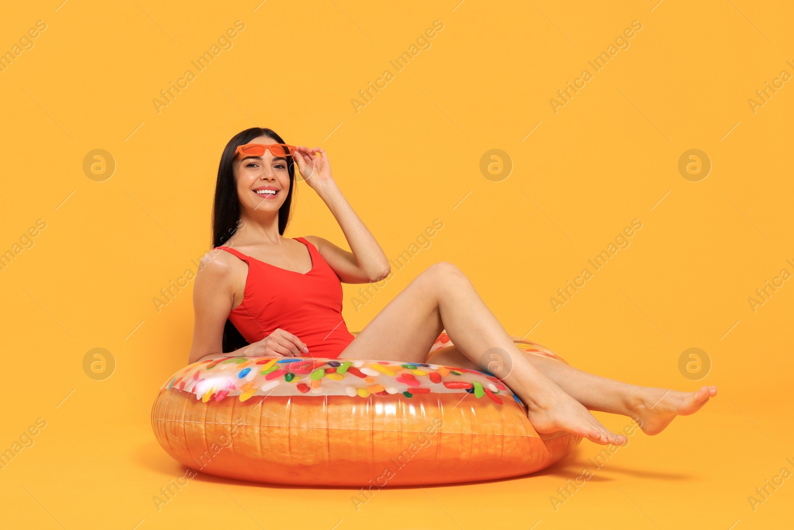 Photo of Happy young woman with beautiful suntan and sunglasses on inflatable ring against orange background